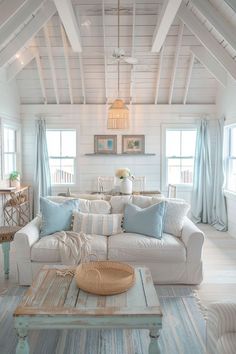 a living room filled with white furniture and blue pillows on top of it's couches