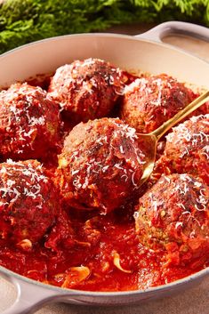 meatballs covered in marinara sauce and parmesan cheese being stirred with a spoon