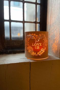 A wood and glass lantern carved with hearts and leaves saying love us lit with a candle. Perfect decor for weddings, and engagements