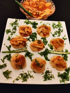 small appetizers are arranged on a white plate with green garnishes