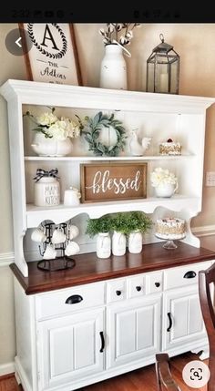 a dining room hutch with white flowers and greenery on the top, along with other decor items