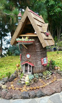 a small tree house made out of wood and rocks in a garden with plants growing on the roof