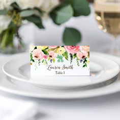 a place card on a plate with flowers and greenery in the background for an elegant table setting