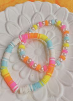 two bracelets on a white plate with yellow and blue beads in the shape of a heart