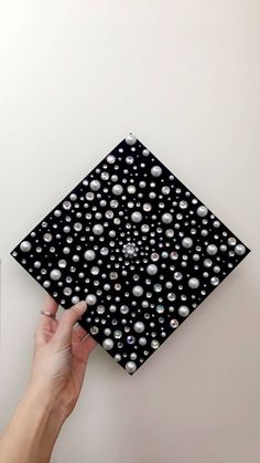 a hand is holding up a black and white square tile with pearls on the bottom