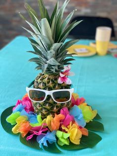 a pineapple with sunglasses on top of it sitting on a blue table cloth at a party