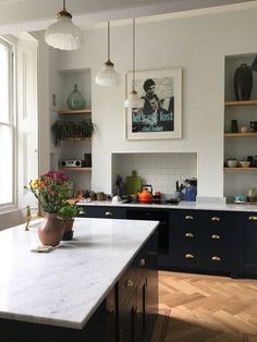 a kitchen with white marble counter tops and black cabinets, two hanging lights above the island