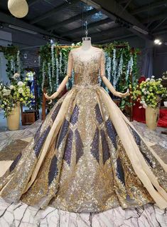 a gold and blue gown on display in a room filled with flower arrangements, flowers and greenery