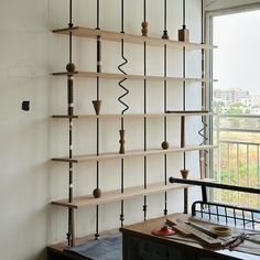 a wooden shelf with many different items on it next to a table and chair in front of a window