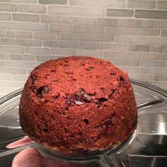 a hand holding a round cake in front of a brick wall on a glass platter