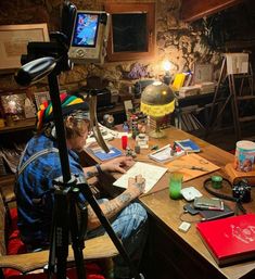 a man sitting at a desk in front of a camera and writing on a piece of paper