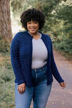 a woman standing on a path in the woods smiling at the camera with her hands behind her back