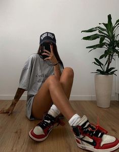 a woman sitting on the floor with her hand up to her face and wearing sneakers