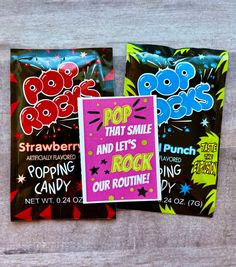 three pops candy bags sitting next to each other on a wooden surface, one with pop that smile and the other with rock our routine