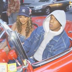 a man and woman sitting in the driver's seat of a red convertible car