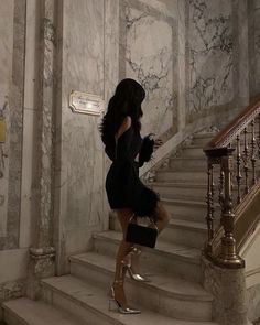 a woman in a black dress is walking down the stairs with her handbag on her hip