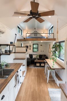 the interior of a tiny home with wood floors and ceiling fans, white cabinets, and wooden countertops