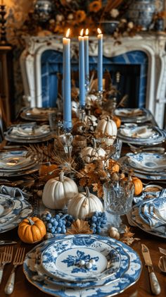 a dining room table set with blue and white plates, silverware and candlesticks