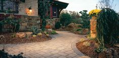 a stone walkway leading to a house with yellow flowers on the front and side of it