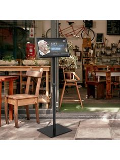 a sign in front of a store with chairs and tables behind it on the sidewalk