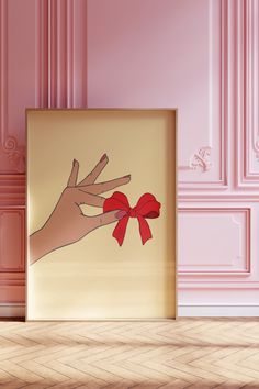 a hand holding a red bow in front of a pink room with pink walls and wooden floors