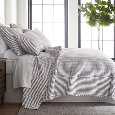 a bed with white and grey striped comforter next to a window in a bedroom