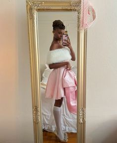 a woman taking a selfie in front of a mirror wearing a pink dress and white fur stole