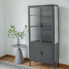 a gray cabinet next to a small table with a vase on it and a potted plant in the corner