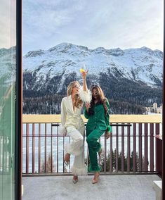 two women standing next to each other in front of snow covered mountains and holding drinks