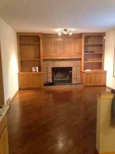 an empty living room with wood flooring and built - in bookcases on either side of the fireplace