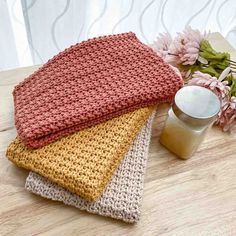 three crocheted dishcloths sitting on top of a wooden table next to flowers