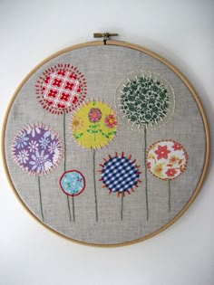 an embroidery project with colorful flowers on the hoop hanging on a wall above a white surface