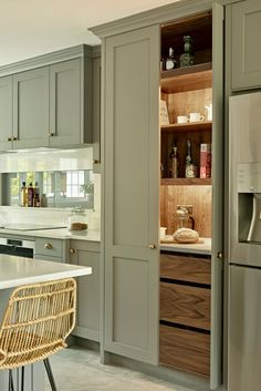 a kitchen with gray cabinets and white counter tops, an island in the middle has a wicker bar stool next to it