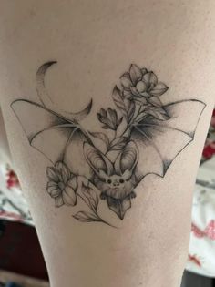 a woman's thigh with flowers and a bat tattoo on the side of her leg