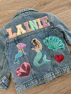 a jeanie jacket with mermaids and hearts on the back, sitting on top of a wooden floor