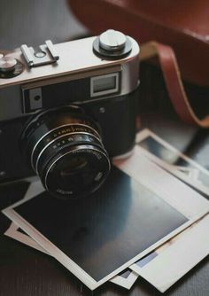 an old fashioned camera sitting on top of several polaroid photos next to a brown leather bag