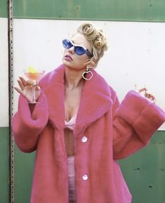 a woman in a pink fur coat holding a drink