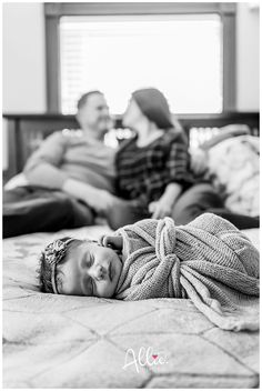 a black and white photo of a baby wrapped in a blanket laying on a bed