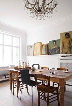 a dining room table and chairs in front of a window with paintings on the wall