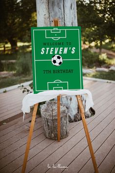 a green sign sitting on top of a wooden easel next to a soccer field