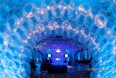 an archway made out of balloons with lights on the ceiling and people in the background