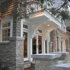 the front entrance to a house with stone steps and columns on both sides, surrounded by pine trees