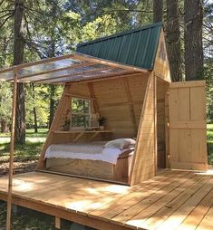 a bed in the middle of a wooden platform with a green roof and windows on it