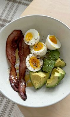 a white bowl filled with bacon, eggs and avocado on top of a table