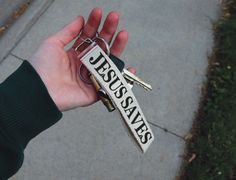 a hand holding a keychain with the word jesus saves on it in front of a sidewalk