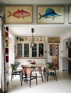 the dining room table is surrounded by four fish paintings on the wall above it's cabinets