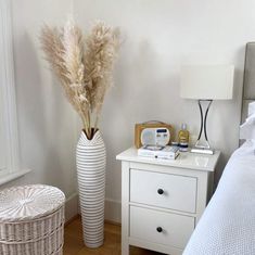 a bedroom with a white bed, nightstand and basket on the floor next to it