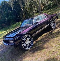 the purple car is parked on the side of the road in front of some trees