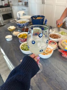 a person holding up a wine glass with eyes painted on it in front of bowls of food