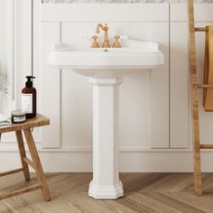 a white pedestal sink sitting next to a wooden stool